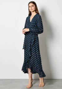 Abito a pois navy con scollatura a V profonda e maniche lunghe. Caratterizzato da un orlo arricciato e un dettaglio in vita con fiocco. Tessuto morbido e fluido.