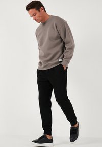 Grijze sweatshirt met een ronde halslijn, lange mouwen en geribbelde manchetten, gecombineerd met zwarte taps toelopende joggingbroek en zwarte sneakers.