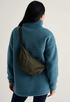 Pīļu zaļas krāsas pūkains flīsa džemperis ar augstu apkakli, kopā ar olīvu zaļu plecu somu ar rāvējslēdzēju. Matētas faktūras visur.