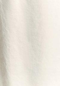 Un tissu beige, texturé, avec une surface légèrement froissée, fabriqué à partir de fibres naturelles, affichant une finition douce et mate.