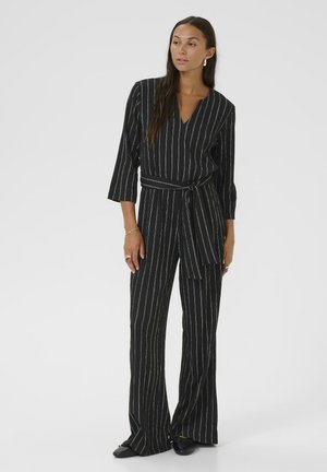 Mono negro con rayas verticales blancas, escote en V, mangas tres cuartos y cintura ceñida con cinturón. Piernas acampanadas, textura suave y diseño minimalista.
