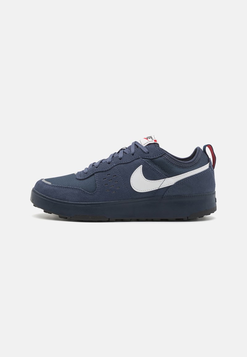 Navy blue sneakers with mesh and suede materials, white Nike swoosh, rounded toe, rubber sole, dark accents, and six eyelets for laces.