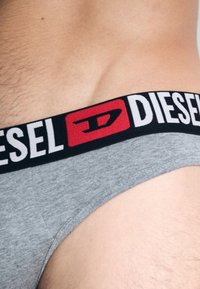 Γκρι βαμβακερό εσώρουχο με μαύρη ελαστική μέση, με έντονα λευκά γράμματα και κόκκινο λογότυπο στο μπροστινό μέρος. Λείο υφασμά, εφαρμοστή σχεδίαση.