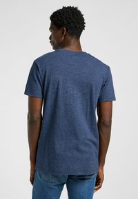 Kortärmad marinblå t-shirt i ett mjukt, texturerat material. Har en klassisk rund halsringning och en avslappnad passform, sedd bakifrån.