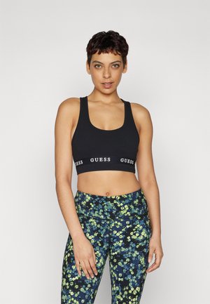 Sujetador deportivo negro con una banda elástica ancha que presenta el logo "GUESS". Combinado con leggings estampados en un diseño floral azul y verde.