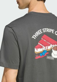 Šedé bavlněné tričko s barevným grafickým motivem kousků dezertu, šálku kávy a borůvek, s textem "TŘI PÁSOVÝ DORT" nahoře.