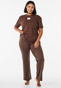 Brunt loungewear-set med en kortärmad skjorta med en rosa logotyp och byxor i ett mjukt, elastiskt tyg.