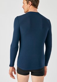 Camicia a manica lunga blu navy realizzata in tessuto morbido, con scollatura rotonda e design aderente, con cuciture sottili lungo le cuciture.