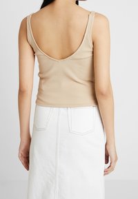 Beige ribbed tank top dengan punggung V dalam, dilengkapi dengan tali bahu yang dapat disesuaikan. Dipadukan dengan rok denim putih, menampilkan kantong belakang dan jahitan.