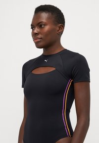 Μαύρο μαγιό κοντό μανίκι με άνοιγμα σε σχήμα κλειδιού, με μωβ και πορτοκαλί ρίγες περιμετρικά και ένα μικρό λογότυπο στο στήθος.