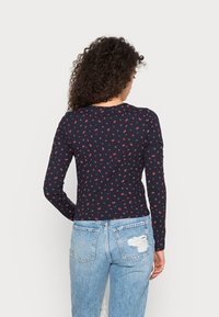 Marineblaues Langarmoberteil mit kleinen roten Blumenmustern. Rippstruktur, runder Halsausschnitt, kombiniert mit hellen, verwaschenen Jeans.