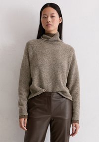 Beżowy sweter z golfem o luźnym kroju, wykonany z teksturowanej dzianiny, w połączeniu z ciemnobrązowymi skórzanymi spodniami.