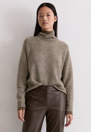 Beiger Rollkragenpullover mit lockerer Passform, aus strukturiertem Strickmaterial, kombiniert mit dunkelbraunen Lederhosen.