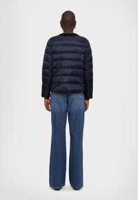 Navy puffer jacket with quilted design, round neckline, and long sleeves; paired with wide-leg blue jeans featuring back pockets.