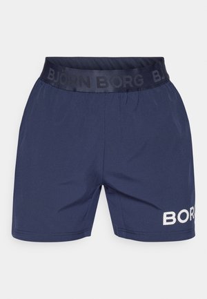 Sötétkék sportnadrág elasztikus derékpánttal, fekete logószalaggal. A bal lábon fehér perforált szöveges logó részlet található.