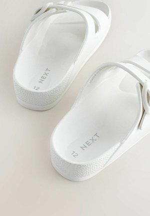 Bílé plastové sandály s texturovanou podrážkou a dvěma překříženými pásky; značka "NEXT" vytištěná uvnitř. Velikost označena jako 12.