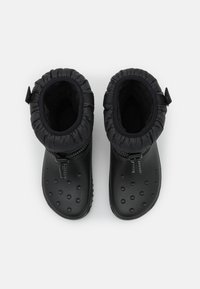 Bottes noires imperméables avec un extérieur lisse, une semelle texturée et un haut à cordon de serrage. Comprend une fermeture éclair et un doublure rembourrée pour le confort.