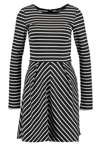 Robe rayée noir et blanc avec des manches longues, présentant un haut ajusté et une jupe évasée avec des rayures diagonales. Fermeture éclair au dos.