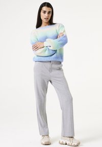 Strickpullover in einem Farbverlauf von Pastellblau und Creme, oversize Passform; kombiniert mit hellgrauen, maßgeschneiderten Hosen und klobigen beigen Sneakers.