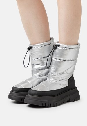 Botine pufos de culoare argintie, cu talpă din cauciuc negru, având o textură matlasată și un șnur ajustabil în partea de sus pentru o fixare confortabilă.