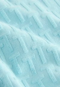 Tejido azul claro con un patrón texturizado que presenta formas de "T" repetidas. Textura suave y tejida con un detalle de costura claro en todo el tejido.