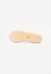 Shoe sole made of light beige rubber, featuring a textured wave pattern and a yellow logo. Smooth edges with a rounded shape.