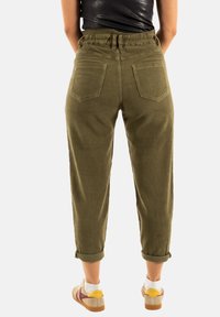 Pantalones de pana verde oliva con un ajuste relajado, cinturilla elástica, puños enrollados y dos bolsillos traseros, presentando un patrón texturizado en relieve.