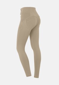 Leggings beiges avec une taille haute, texture lisse et poches cousues à l'arrière, présentant un design ajusté et des coutures plates.