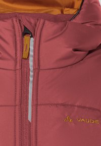Burgundia värvi pehmendatud jakk, millel on metallist tõmblukk, oranž vooder ja broderitud logo. Sellel on õmmeldud paneelid ja soe krae.