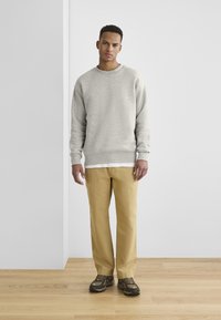 Lys grå hettegenser med ribbede mansjetter og nederkant, sammen med beige løse bukser. Brune joggesko med en robust såle fullfører antrekket.