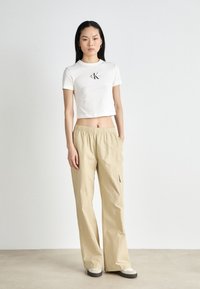 Kortgesneden wit T-shirt met geborduurd logo, gecombineerd met lichtbeige cargobroek met elastische tailleband en zijzakken.