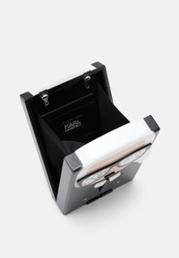 Czarna, błyszcząca torba w kształcie pudełka z odpinanym wnętrzem, srebrnymi akcentami i grafiką okularów z przodu; posiada zapięcie na zatrzask.