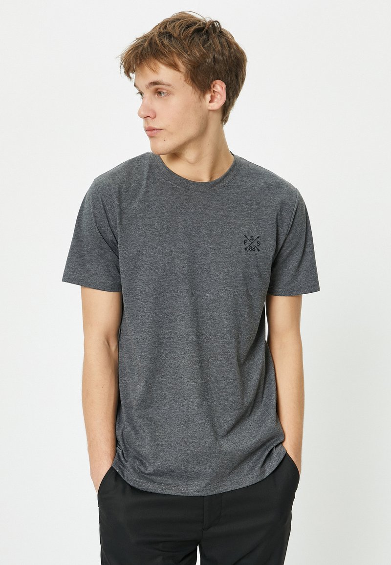 Grå kortærmet t-shirt lavet af blødt stof, med et lille sort logo på venstre bryst. Crew neck design med en afslappet pasform.