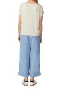 Witte korte mouwen top gecombineerd met lichtblauwe wijde broek en witte sneakers met zwarte accenten; gladde stof met een relaxte pasvorm.