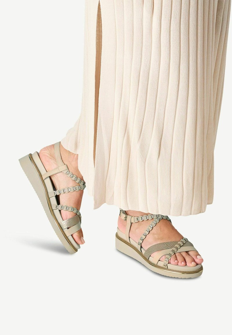 Grüne Leder-Sandalen mit mehreren Riemen-Designs, featuring geflochtene Akzente und eine strukturierte Fußbett, kombiniert mit einem plissierten beigen Rock.