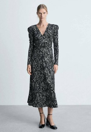 Schwarz-weiß gemustertes Kleid mit langen Ärmeln, V-Ausschnitt und gerafften Schultern, das knielang ist und einen fließenden Rock hat.