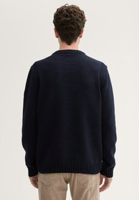 Pull en maille bleu marine avec des poignets et un ourlet côtelés. Présente un col rond classique et une texture subtile sur l'ensemble du tissu.