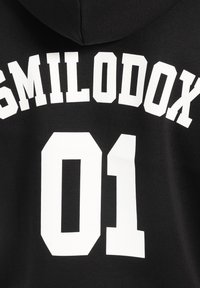 Czarna bluza z kapturem z dużymi białymi literami w stylu blokowym, które brzmią "SMILODOX" oraz numerem "01" z tyłu. Gładka tekstura tkaniny.