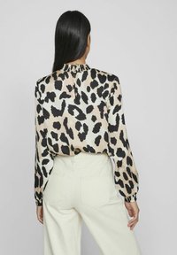Blouse en soie à imprimé léopard noir et beige, dotée d'un col montant et de poignets élastiques, associée à un pantalon large crème.