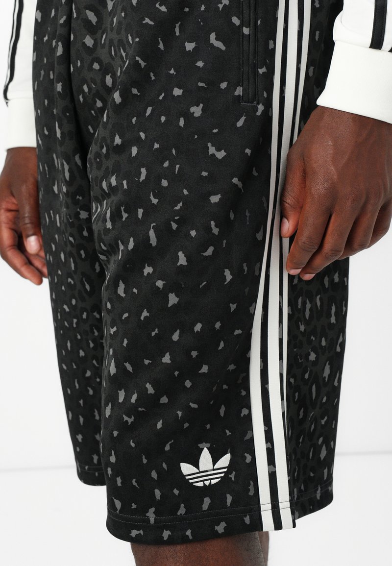 Czarne spodenki sportowe z szarym nadrukiem w panterkę, z białymi paskami po bokach i logo Adidas na dolnej krawędzi. Wykonane z gładkiego materiału.