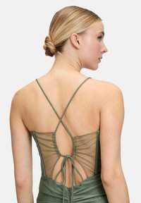 Zielona sukienka z materiału z cienkimi krzyżującymi się ramiączkami, przezroczystym siateczkowym tyłem i zapięciem na wstążkę. Teksturalne wykończenie z delikatnym błyszczącym akcentem.