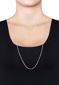 Sølv kædanne med en tvistet design, båret af en person med en sort top, der har en glat tekstur og en subtil reflekterende finish.
