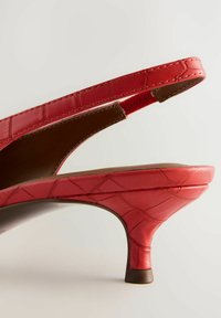 Röda slingback-hälar har en strukturerad yta med krokodilskinnseffekt, en avsmalnande form och en liten blockklack. Insidan är brun.