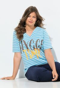 Modro-bílý pruhovaný V-krk tričko s textem "HYCC TIME" v hnědé a oranžové barvě, spárované s tmavě modrými kalhotami. Hladká tkanina a uvolněný střih.