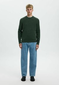 Maglione verde a maglia con collo rotondo, maniche lunghe e orlo a coste, abbinato a jeans a gamba larga di colore blu chiaro e scarpe nere.