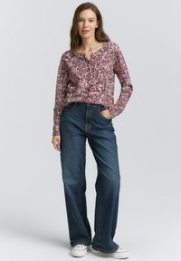 Blouse à manches longues maroon et blanche à motifs avec un col rond, associée à un jean large bleu foncé et des baskets blanches.