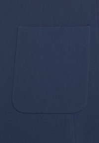 Stevige marineblauwe stof met een groot, afgerond rechthoekig opgestikt zakje.