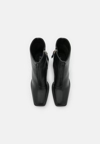 Bottes pour homme en cuir noir à la cheville avec un bout carré et des fermetures éclair sur le côté. Texture lisse avec un design ajusté, silhouette minimaliste.