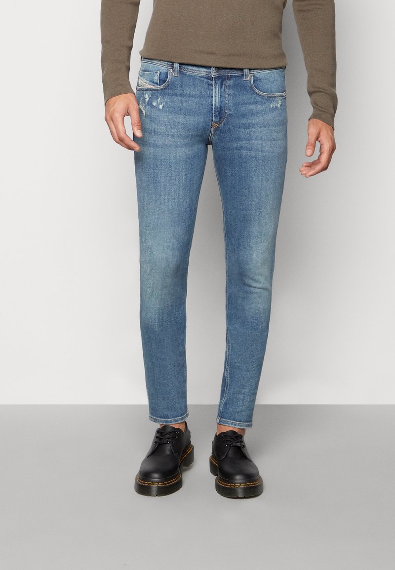 Jeans ajustados de algodón en azul claro, con zonas desgastadas, diseño de cinco bolsillos y un ligero desgarro. Combinados con zapatos negros de cordones.