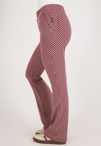 Rode en roomkleurige flared broek met een geometrisch driehoekpatroon en een fitted tailleband. Het materiaal lijkt rekbaar en comfortabel te zijn.
